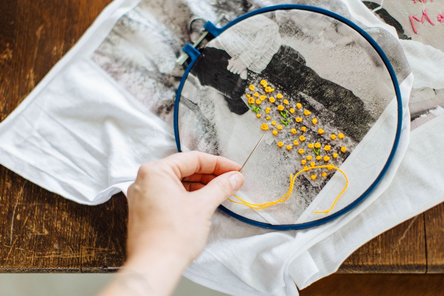 Hands working on embroidering yellow details onto vintage photographs.