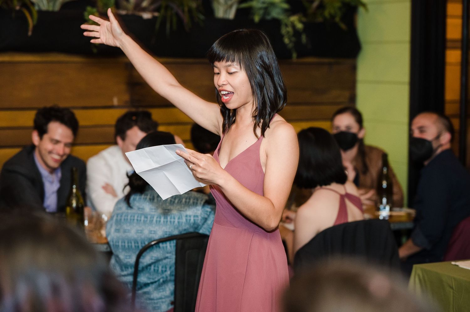 A person in a pink dress sings passionately during a lively gathering.