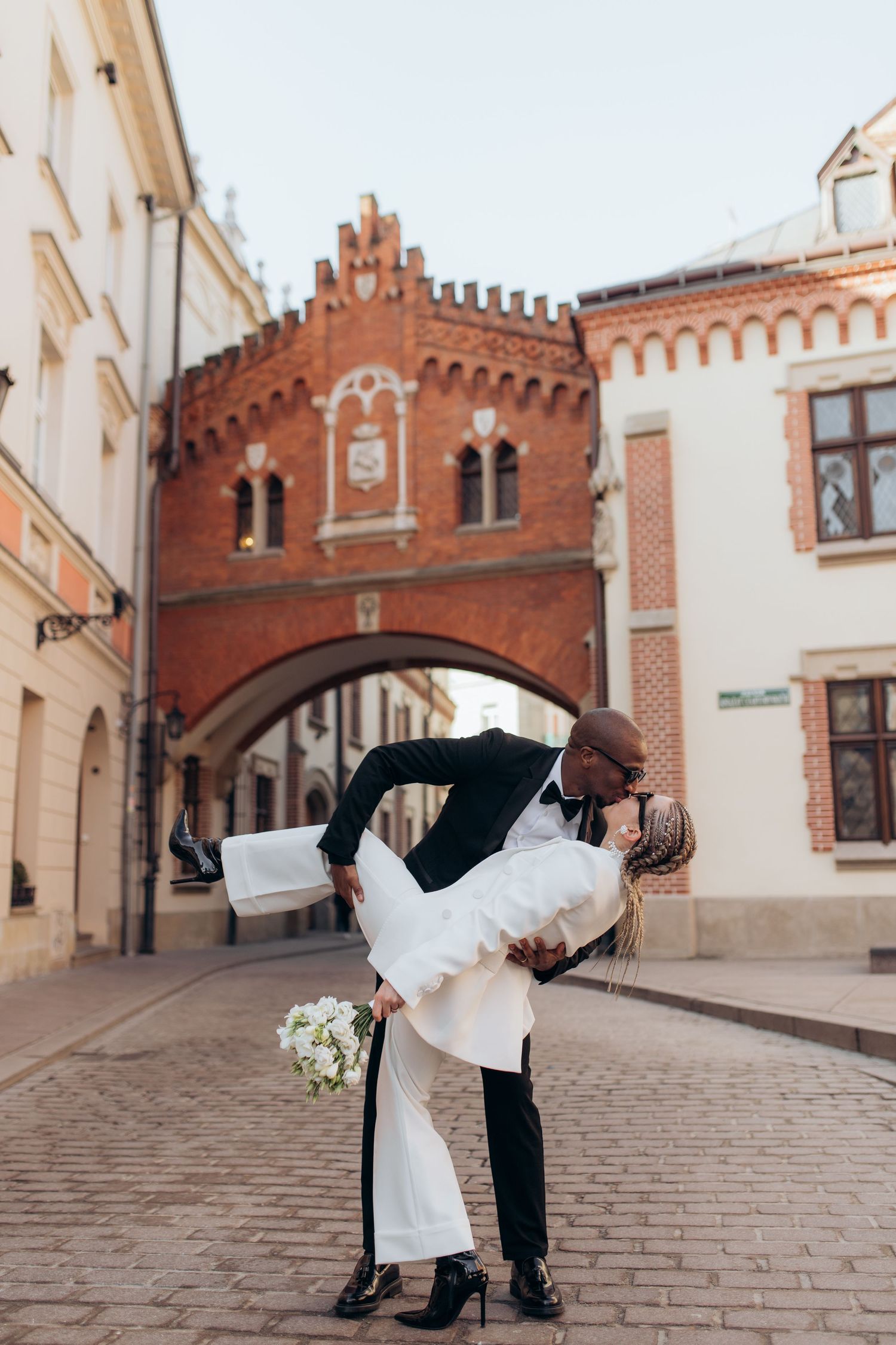 Romantic wedding dip pose in front of historic brick archway in European city.