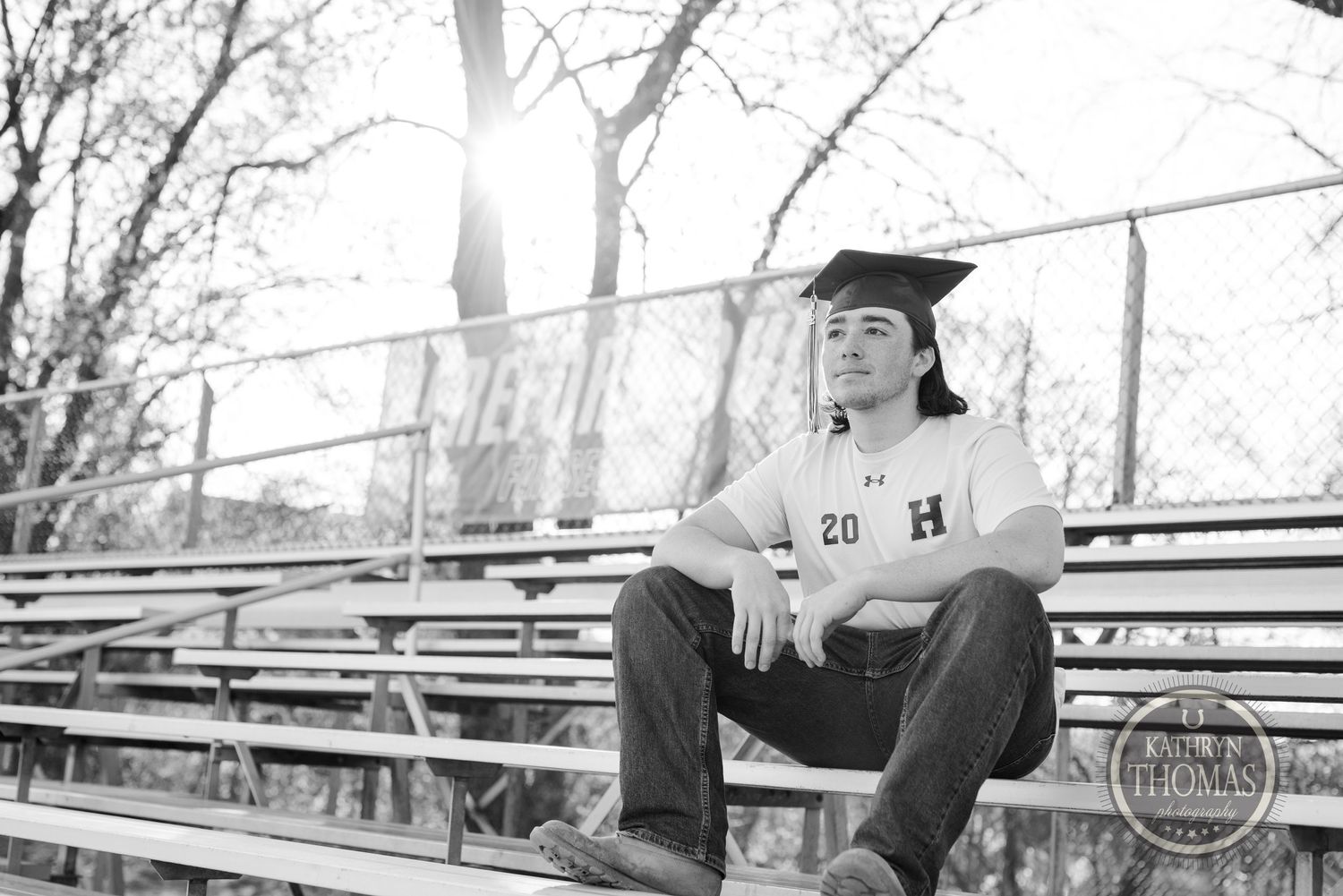 Black and white image of graduate in cap sitting on bleachers during outdoor photo session.