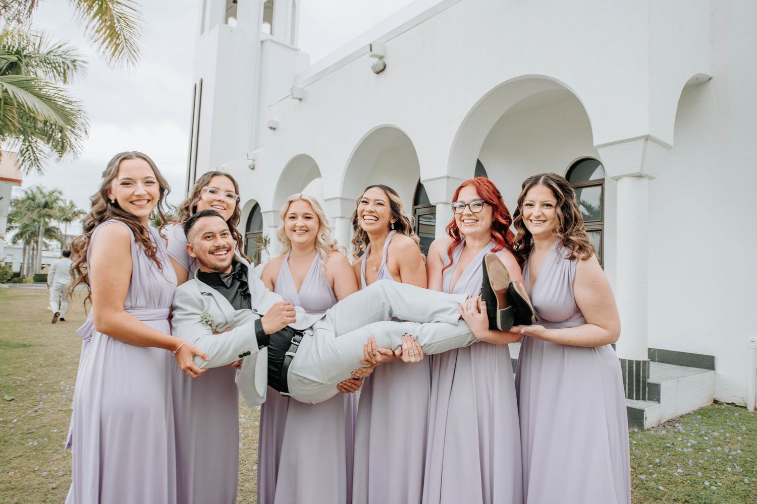 Bridesmaids in lavender dresses gather for a fun group photo outside.