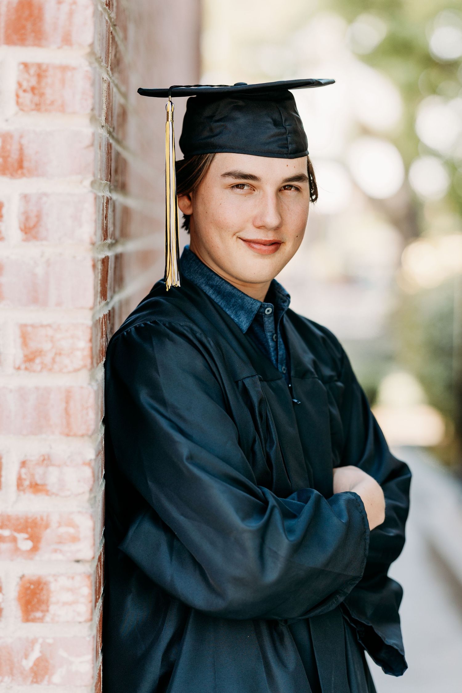 High school senior pose with arms crossed and leaning on a brick wall.