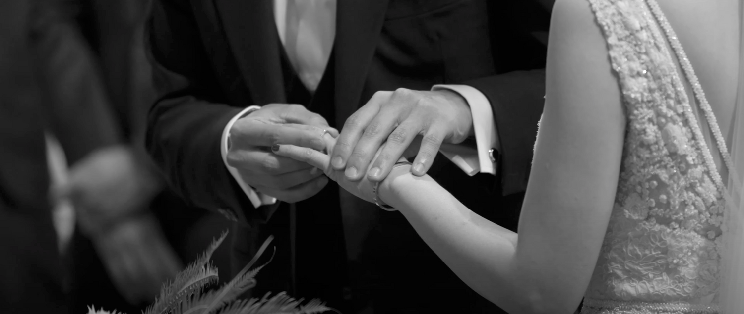 Black and white close-up of couple exchanging wedding rings during ceremony.