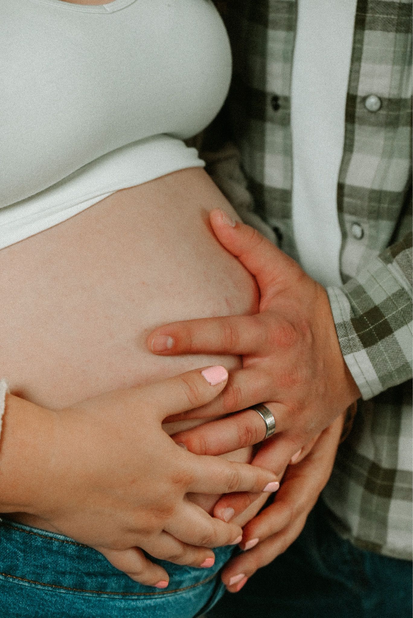 Close-up maternity photo of hands forming heart shape on pregnant belly.