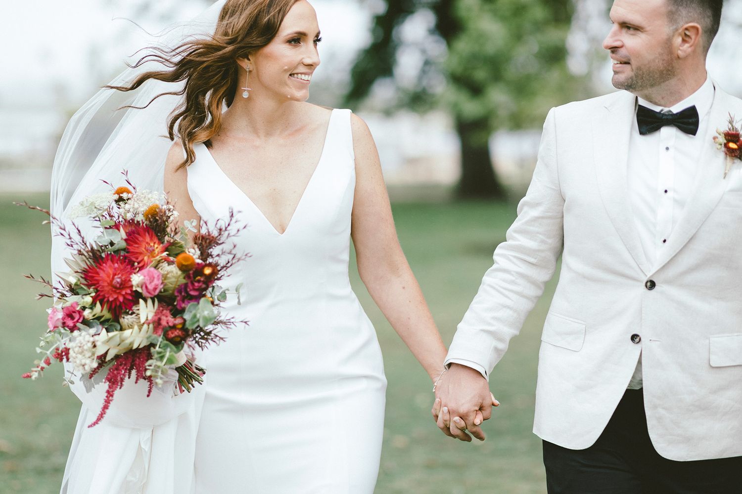 Couple in formal white attire share intimate moment outdoors during wedding celebration.