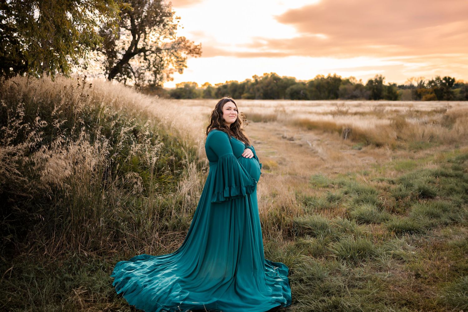 cherry creek trail parker maternity photoshoot, pregnant woman in long green dress, she is cradling her bump, sunset