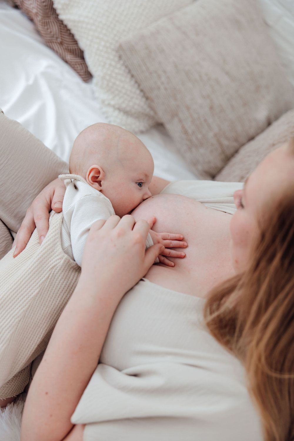 Intimate breastfeeding photograph with baby in neutral tones against white bedding.