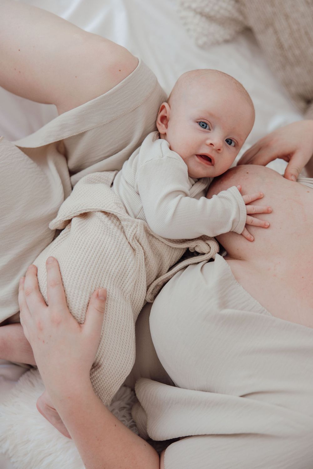 Close-up of baby in cream-colored outfit resting on soft bedding.