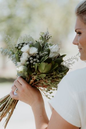 Bride holding natural bouquet of white flowers and greenery in outdoor setting.