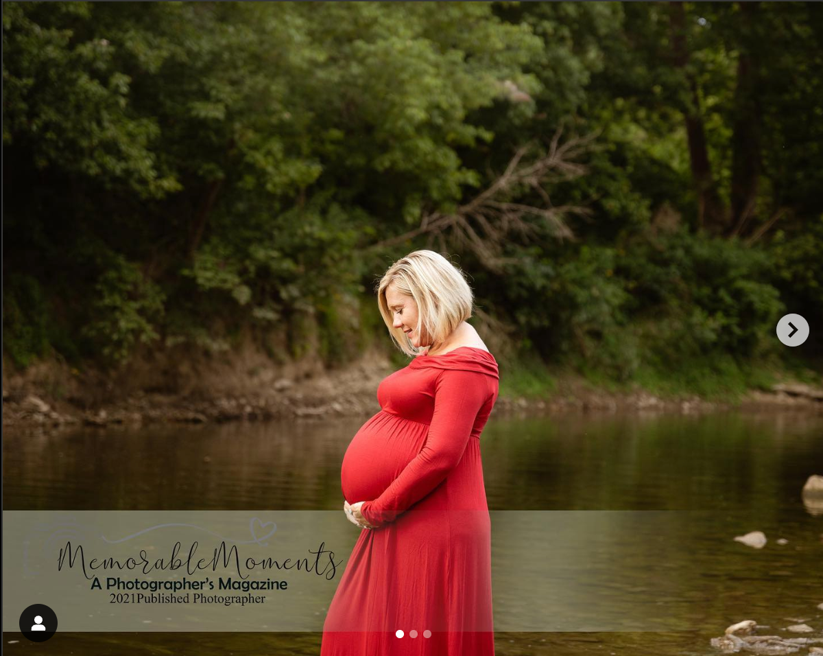 Maternity portrait by a lake with a woman in a red dress amid nature.