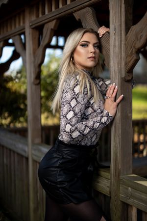 Person in snakeskin print top poses dramatically against wooden gazebo structure.
