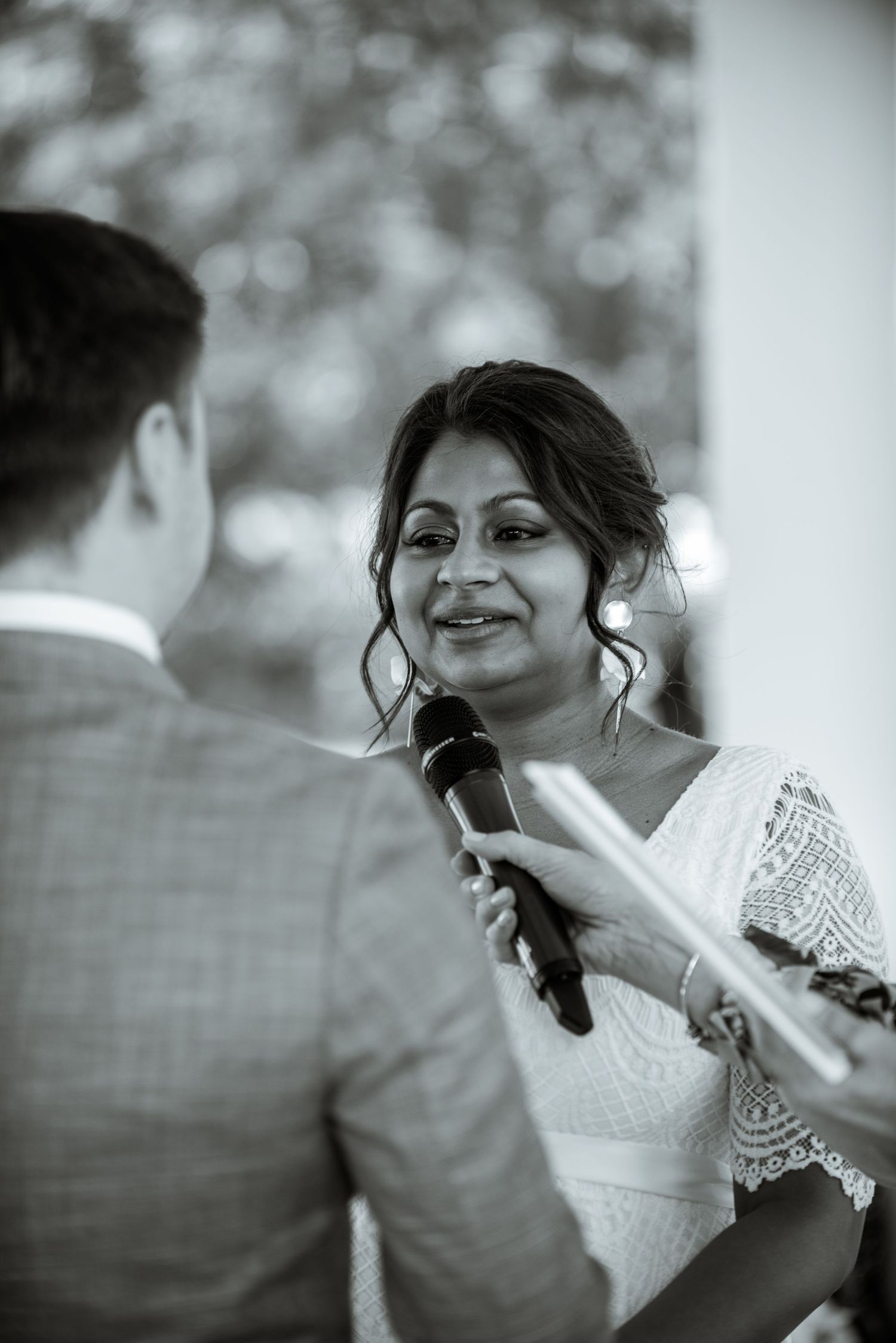 A tender moment during a wedding ceremony as the bride recites vows while holding a microphone.