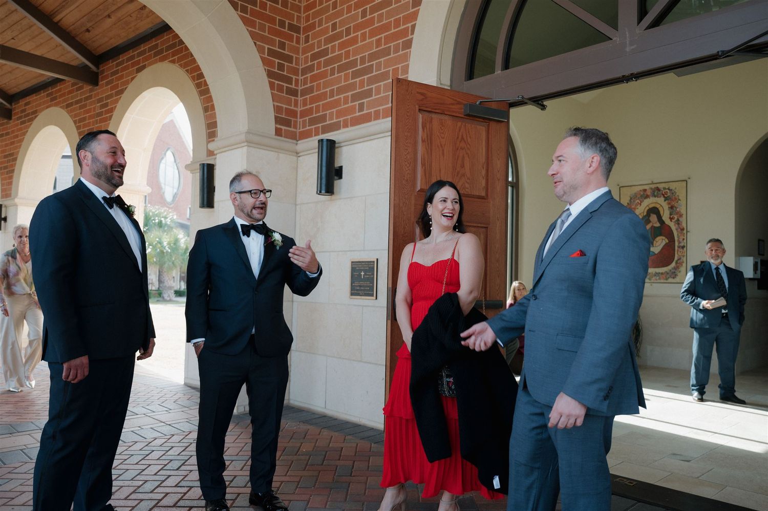 Wedding guests in formal attire conversing under an elegant columned archway.