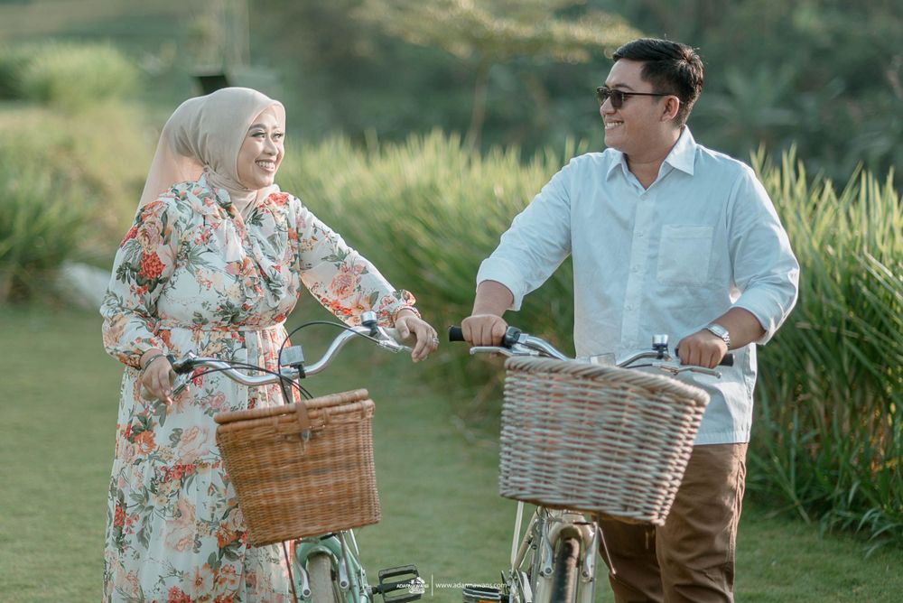 A couple rides vintage bicycles with wicker baskets through a lush outdoor setting.