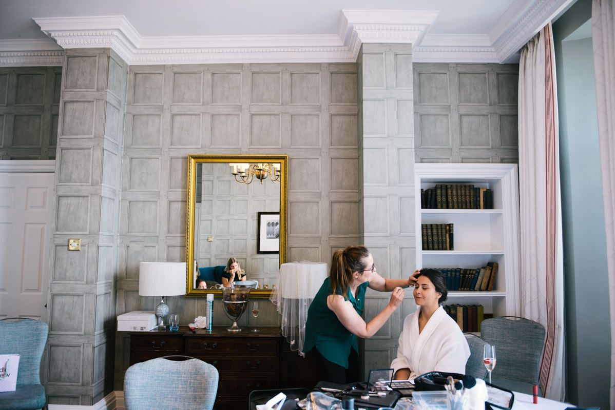 Wedding prep scene in an elegant room with gray paneled walls and a gold mirror.