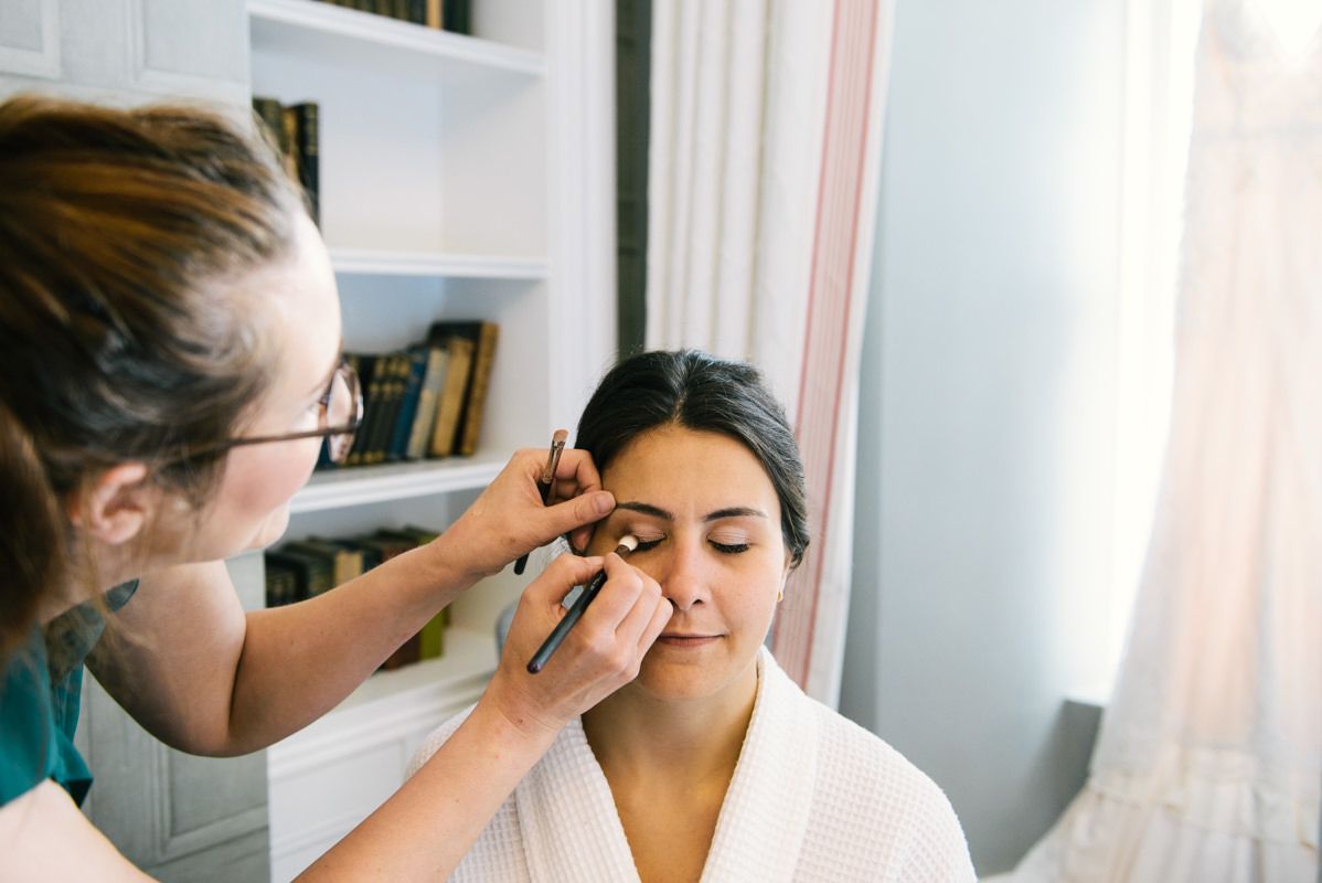 Wedding day makeup preparation scene in a bright, sunlit room.