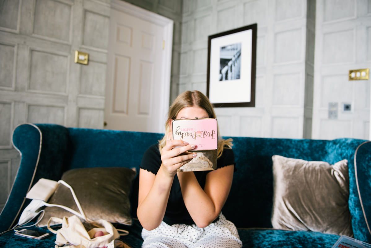 Someone holding a pink greeting card while sitting on a teal velvet couch with throw pillows.