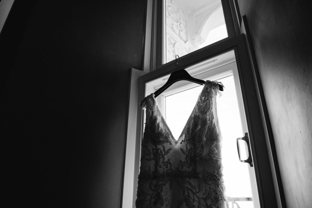 A lace wedding dress hanging in a window silhouetted against bright light.