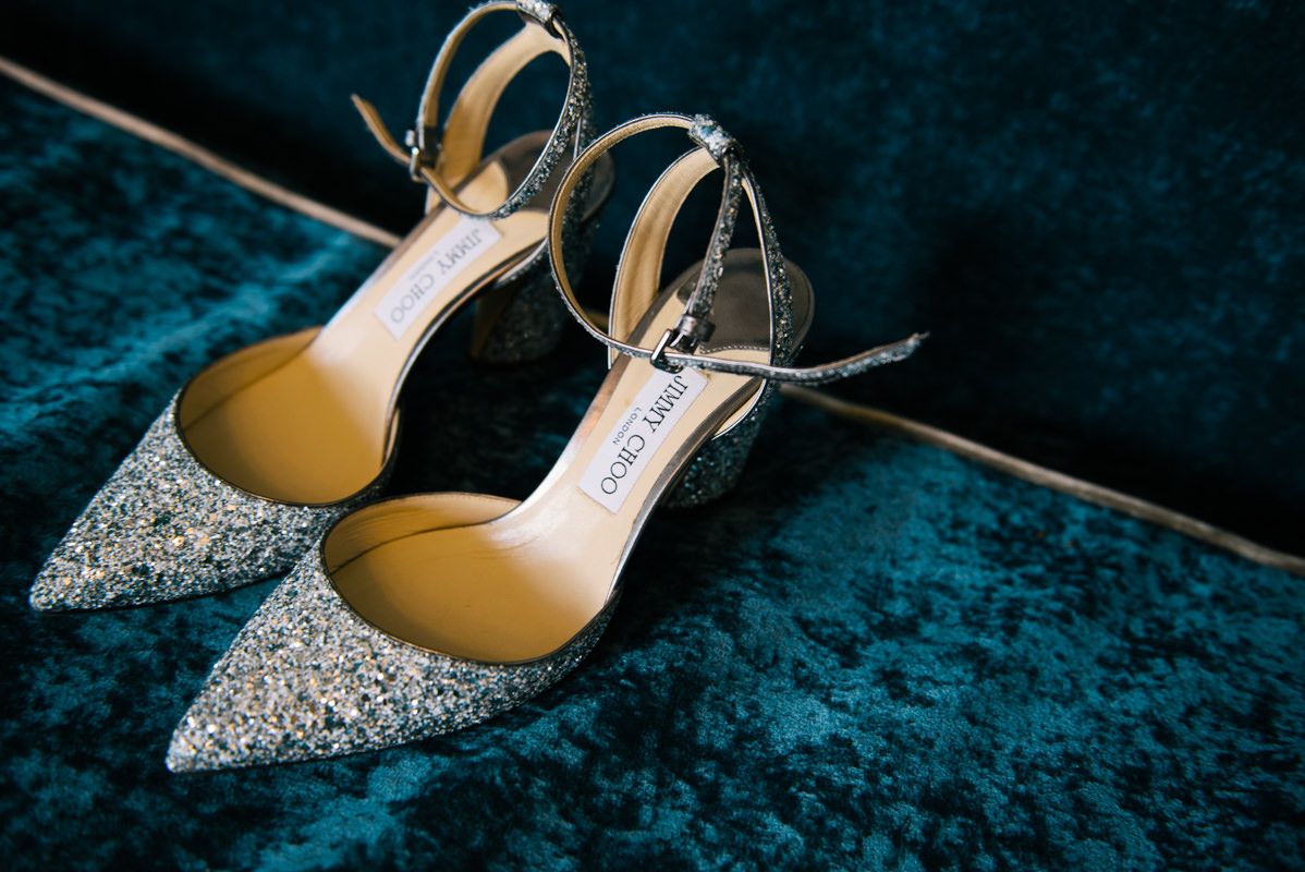 Sparkly silver Jimmy Choo bridal shoes displayed on blue velvet fabric.