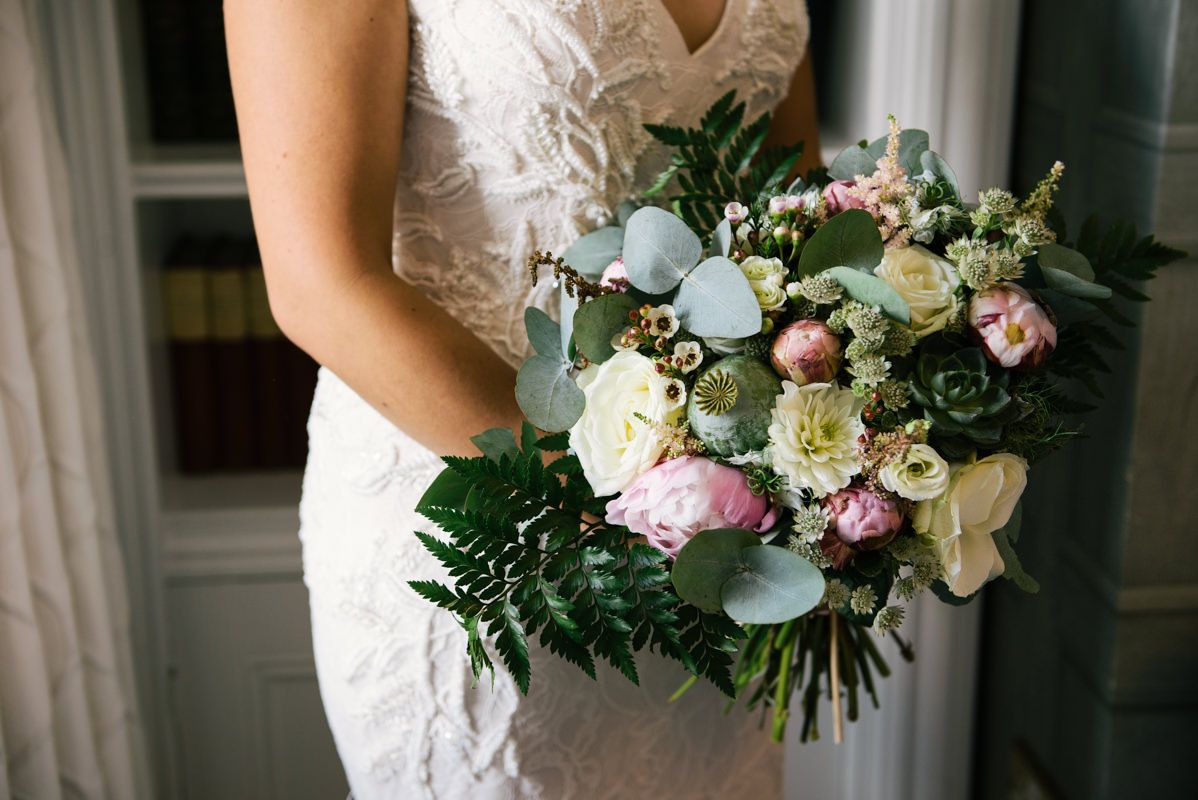 Bride holding an elegant bouquet of pink and white roses with eucalyptus leaves.