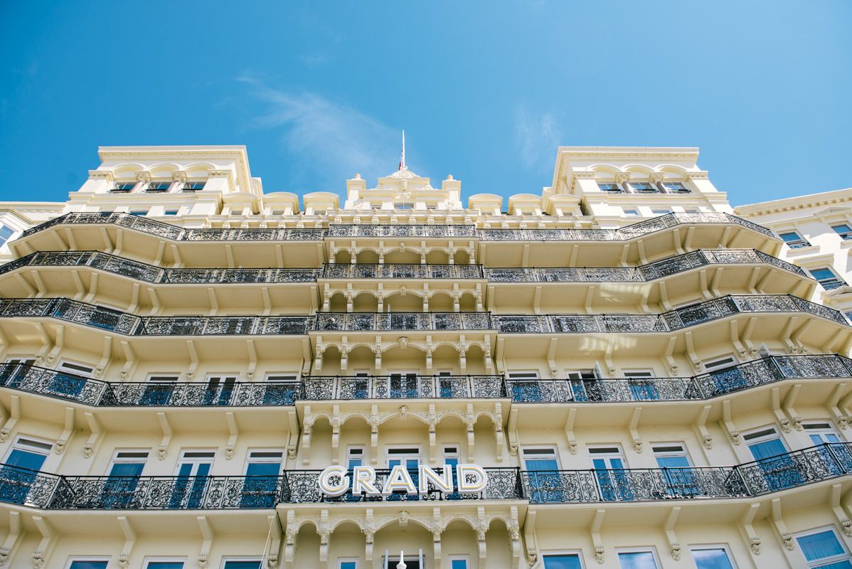 Elegant cream-colored hotel building with ornate balconies against bright blue sky.