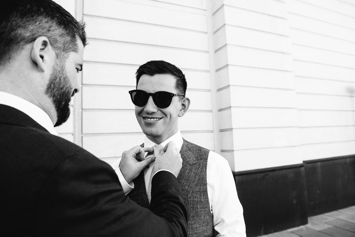 Two people in formal attire adjusting a tie in black and white.