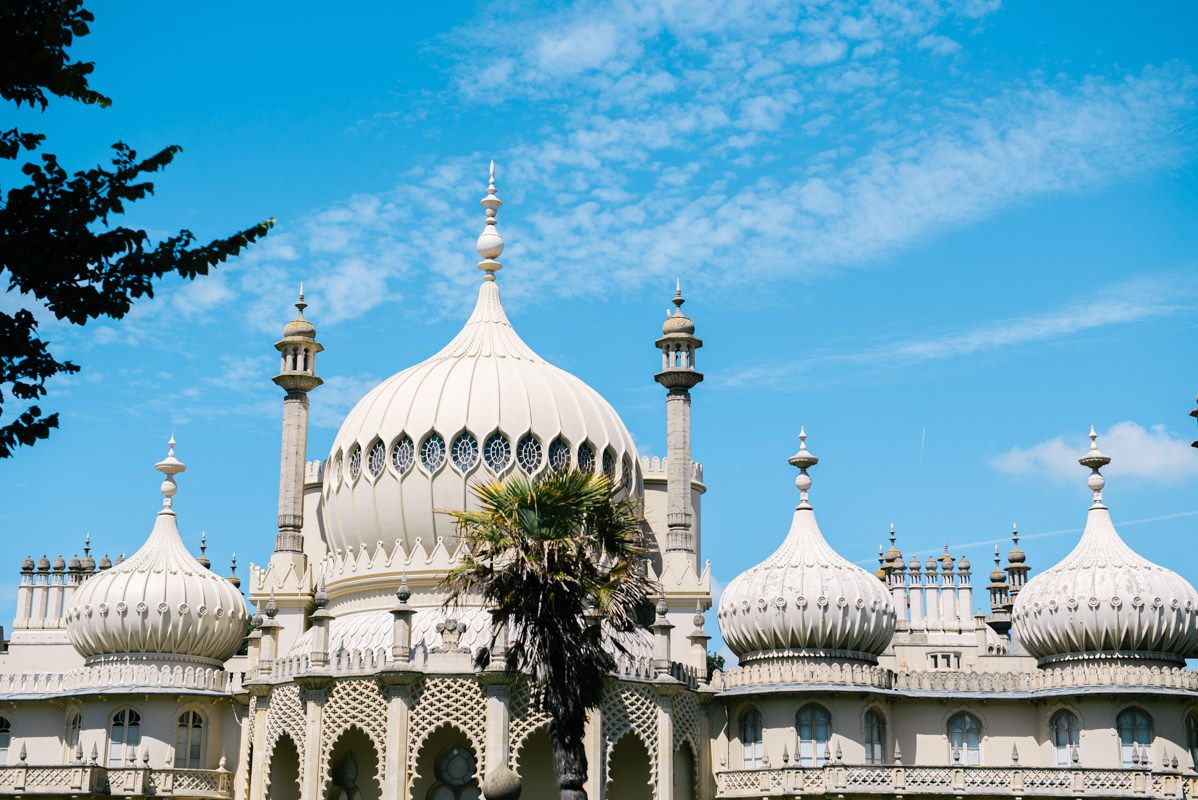 The Royal Pavilion in Brighton features ornate white domes and minarets against a bright blue sky.