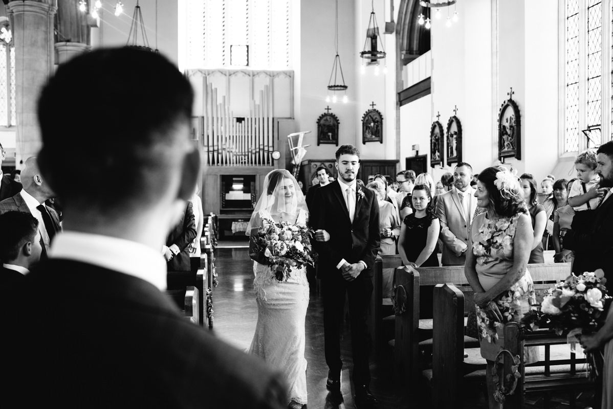 Black and white photo of a wedding ceremony in a historic church with tall windows.