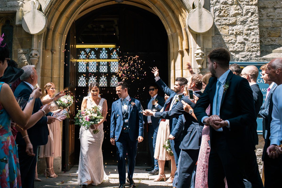 Wedding celebration with guests tossing confetti outside an ornate church entrance.