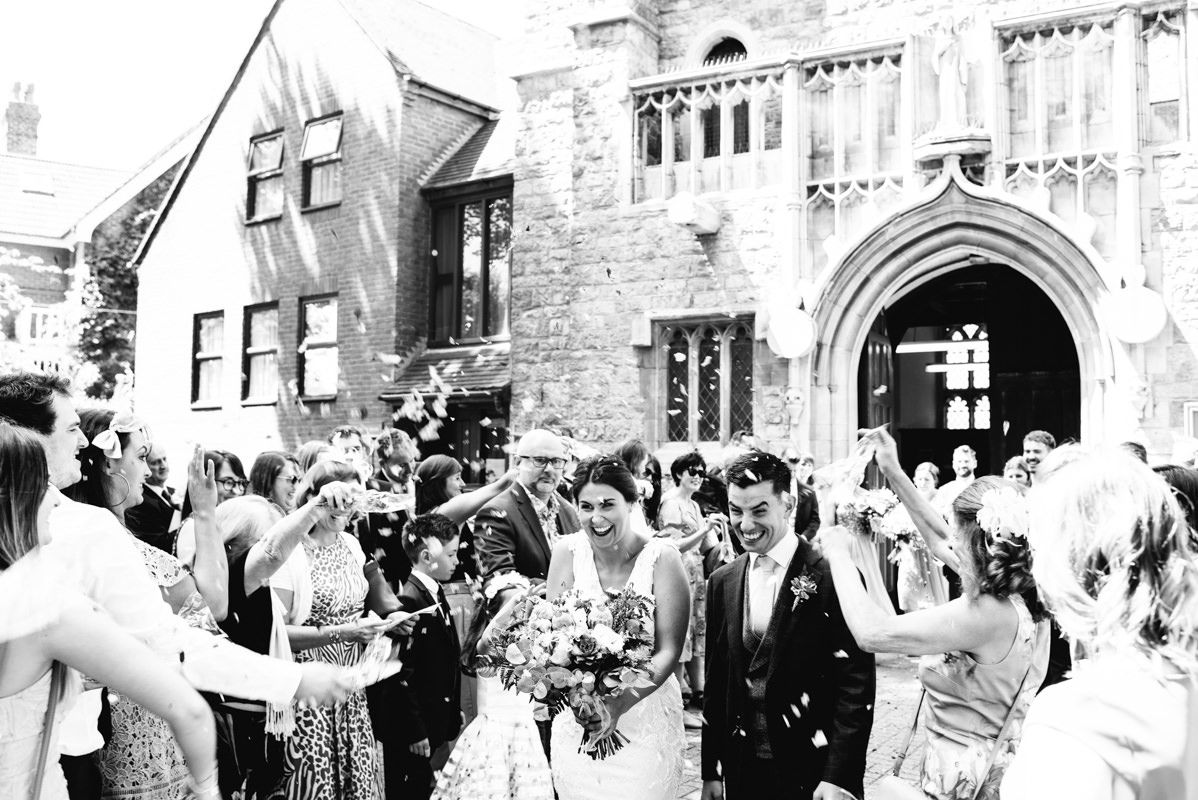 Wedding party celebrating with confetti outside a historic stone church with Gothic arched doorway.