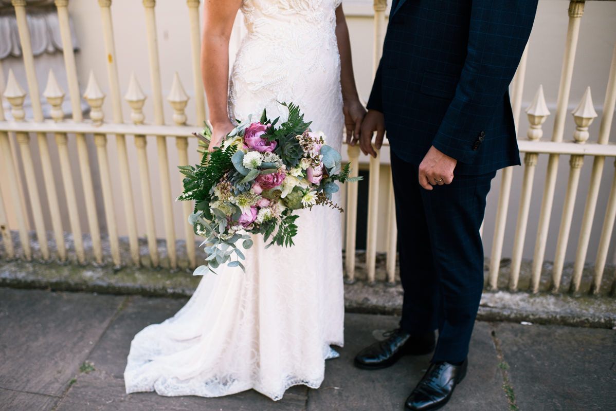 Detail shot of wedding dress and bouquet against white fence backdrop.