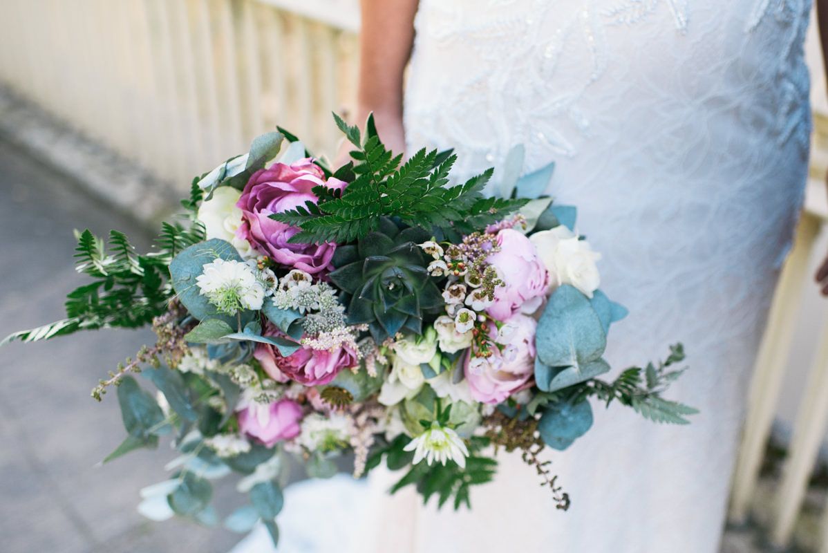 A lush wedding bouquet featuring pink and purple flowers with eucalyptus and green foliage.