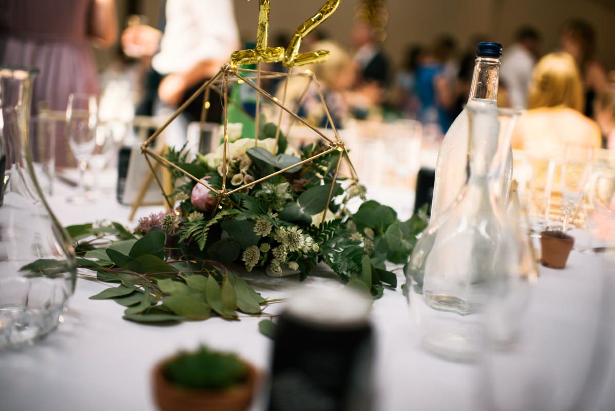 Elegant table setting with greenery centerpiece and glassware for wedding reception.