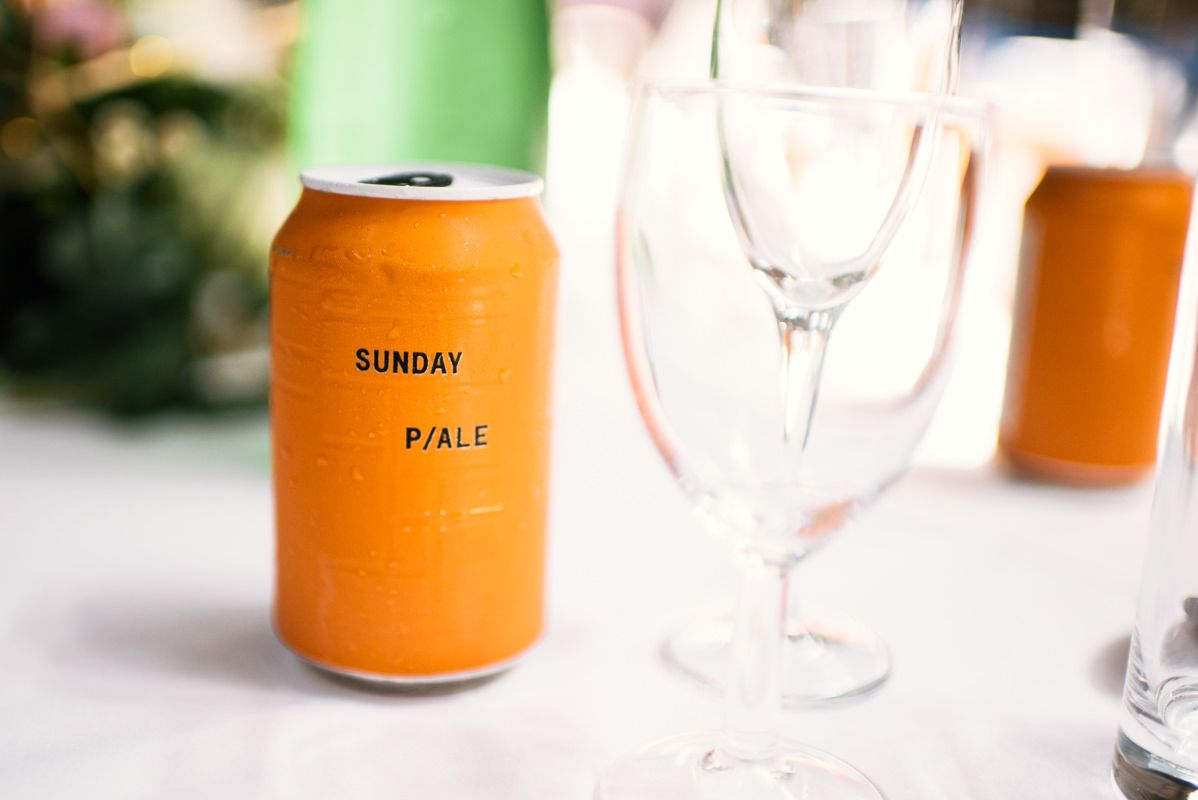 Orange can of Sunday Pale beverage next to empty wine glass on white tablecloth.