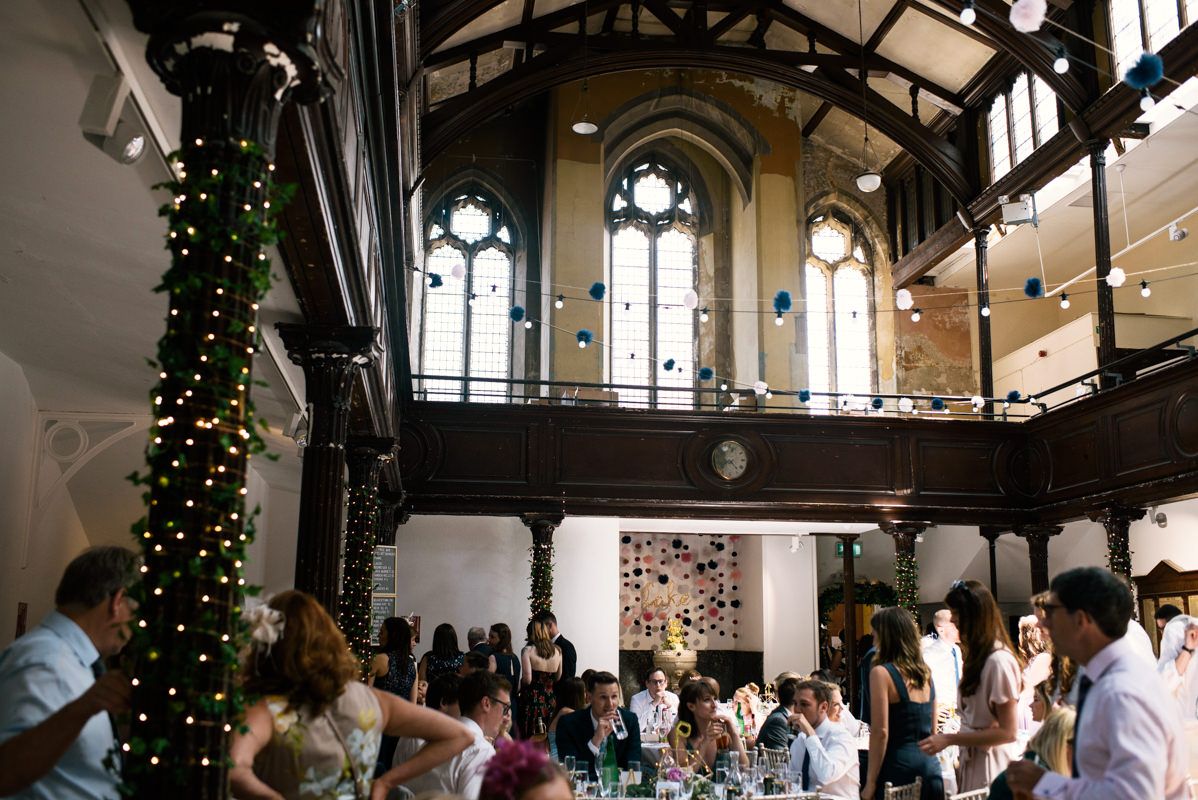 Gothic-style wedding venue with high arched windows, Christmas lights and gathered guests.