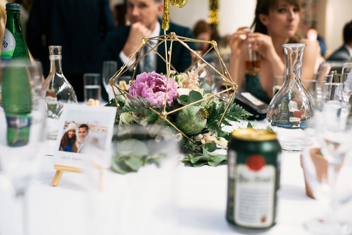 Elegant wedding table setting with geometric floral centerpiece, wine bottles and place settings on white tablecloth.