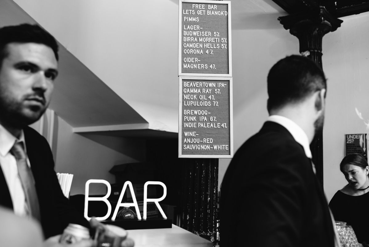 Black and white photo of a modern bar interior with menu boards and staff.