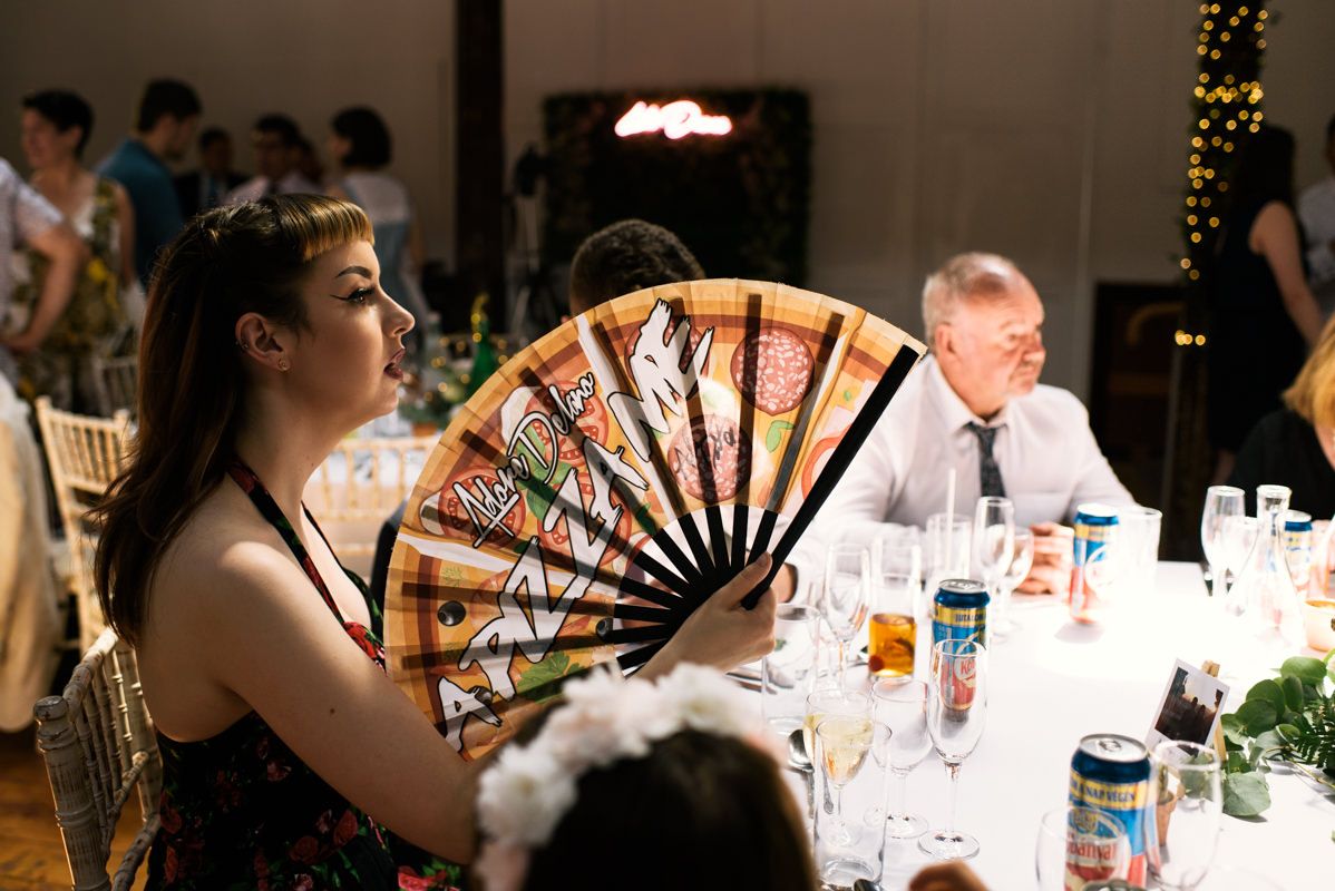 Guest at wedding reception holding decorative fan while sitting at dining table.