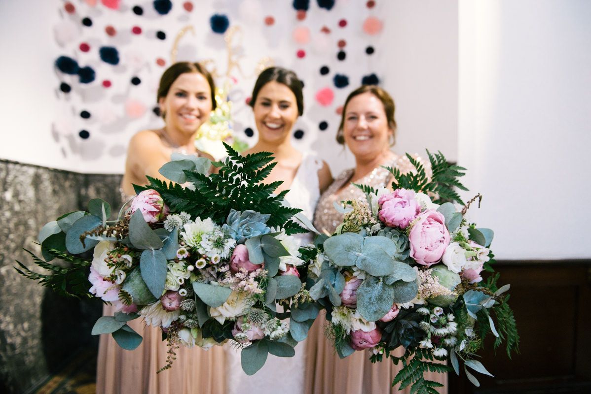 Three bridesmaids holding lush bouquets with eucalyptus and pastel flowers.