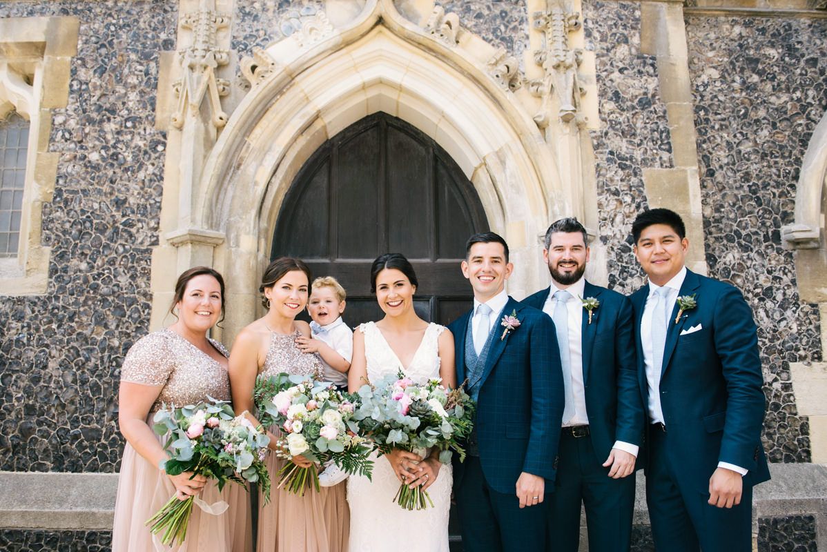 Wedding party standing in front of stone church with gothic arched doorway.