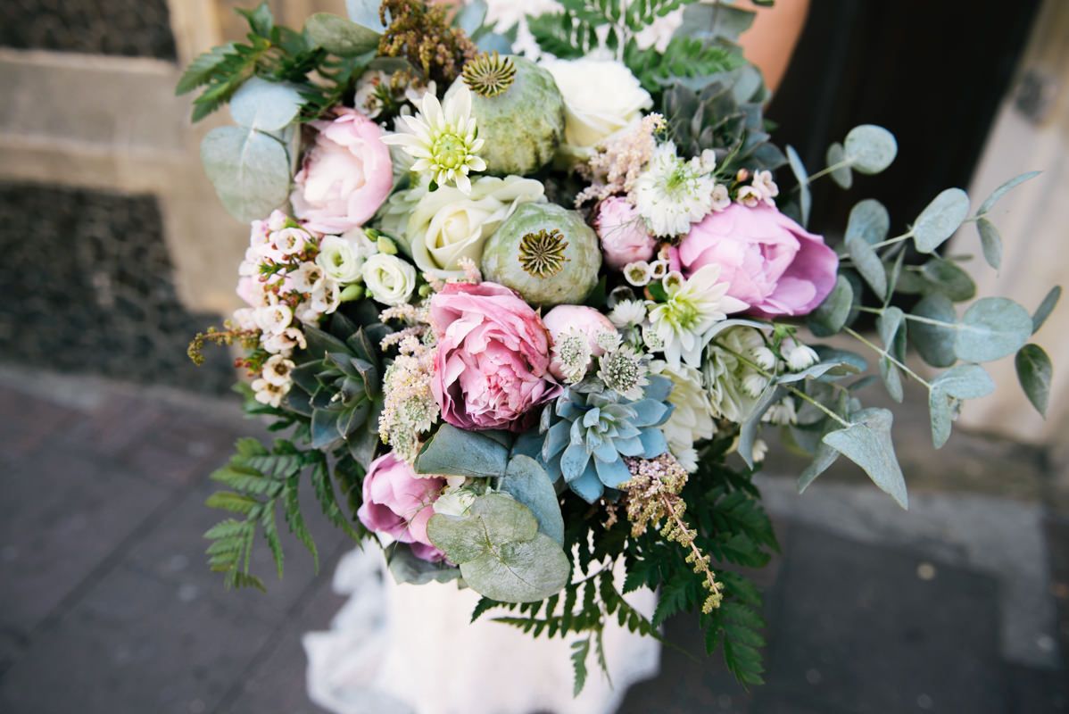 Close-up of an elegant bridal bouquet with pink peonies, white roses, and silvery eucalyptus leaves.