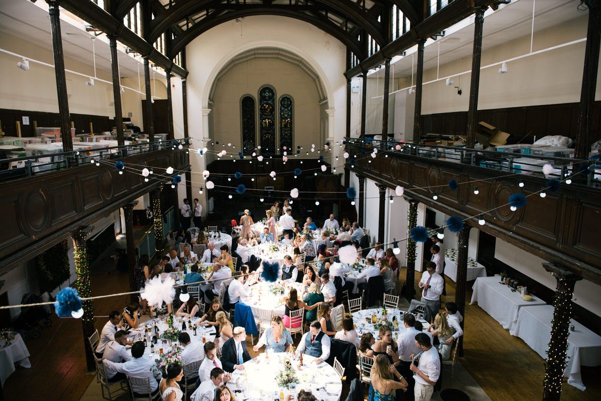 A grand wedding reception venue with high ceilings and balconies filled with dining guests.