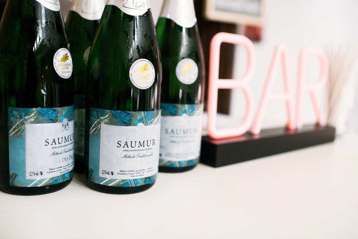 Row of Saumur wine bottles with custom labels displayed near a decorative bar sign.