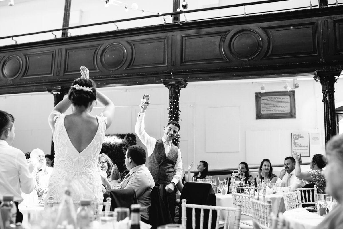 Black and white photo of wedding reception guests celebrating in a traditional venue.