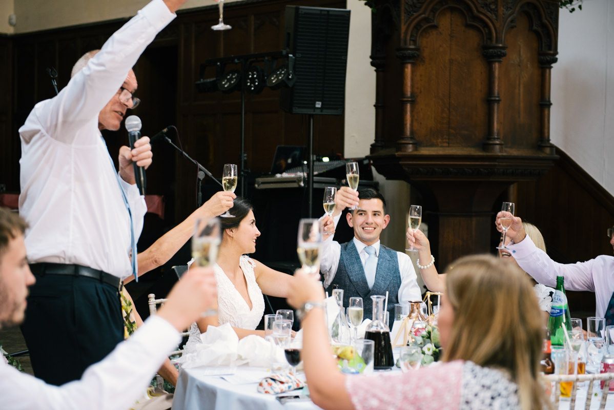 Wedding guests raise their glasses in a celebratory toast during a reception in an elegant indoor venue.