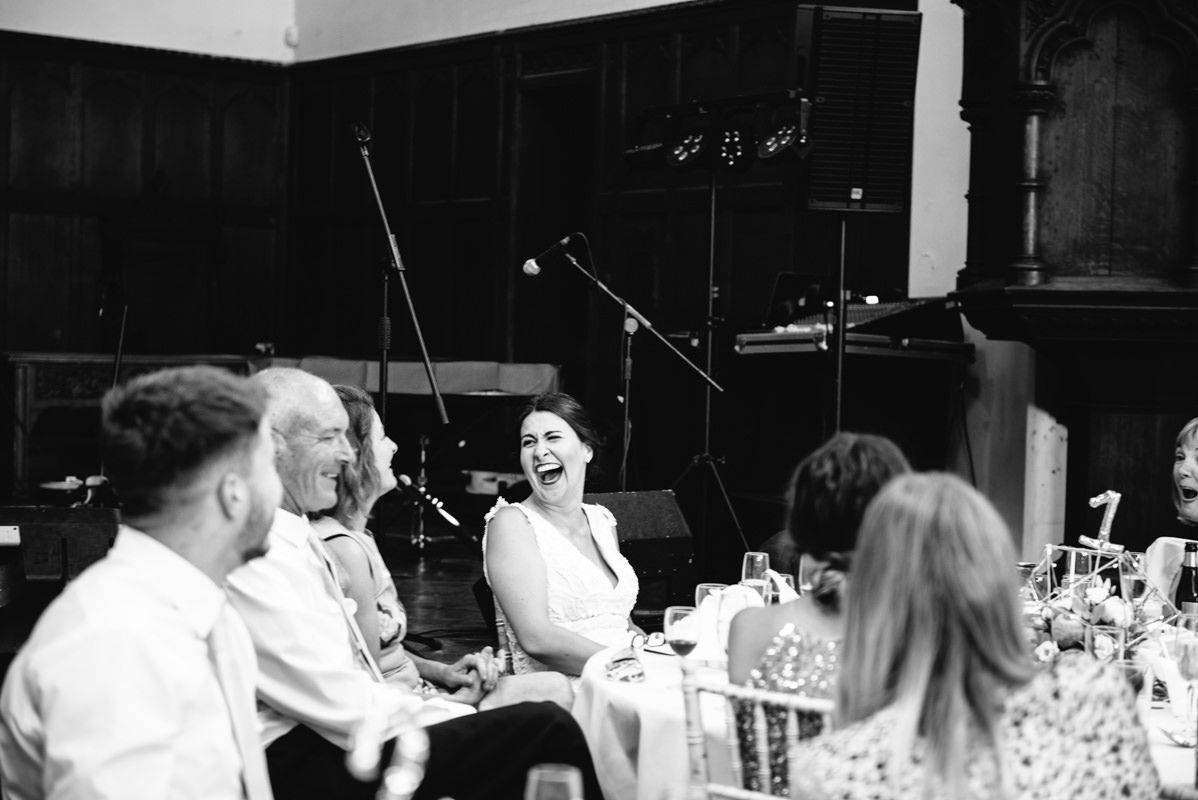 Black and white photo of wedding guests laughing and enjoying speeches during reception.