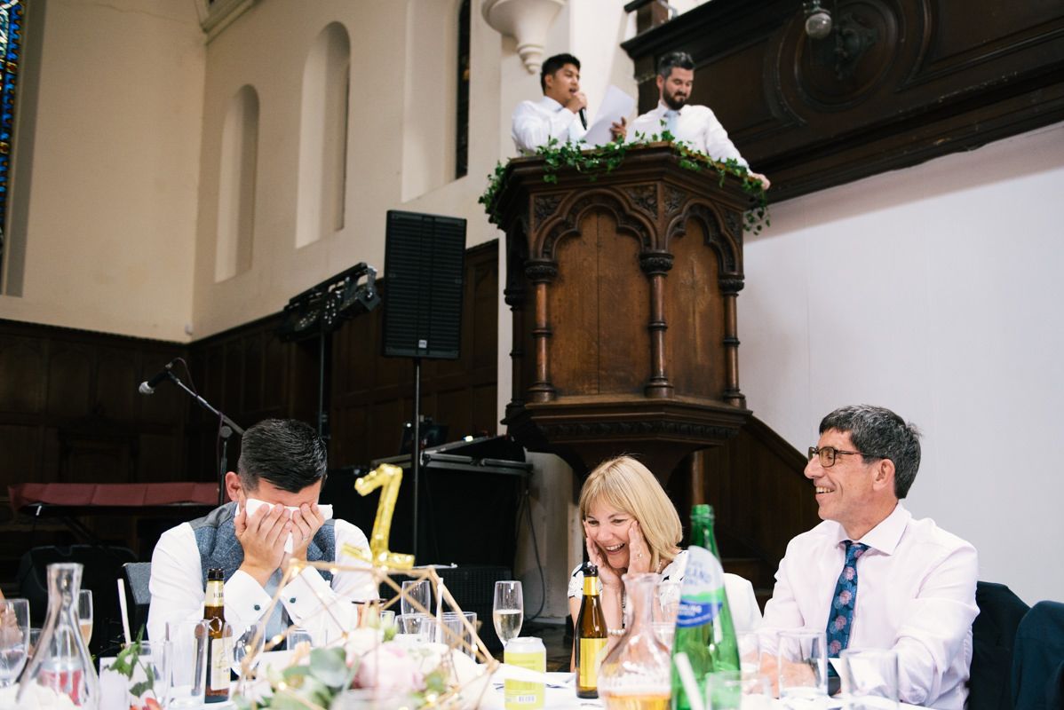 Speakers deliver wedding toasts from decorative wooden pulpit while guests enjoy reception below.