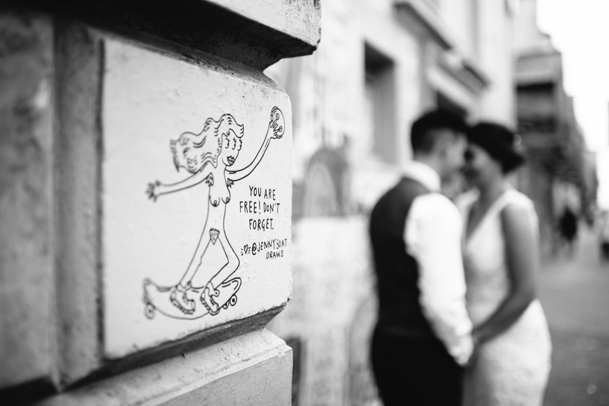 Artistic black and white wedding portrait with street art in soft focus background.
