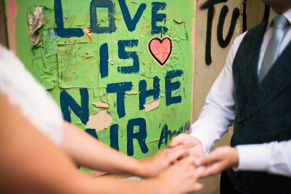 Close up of couple holding hands in front of green graffiti wall with love message.