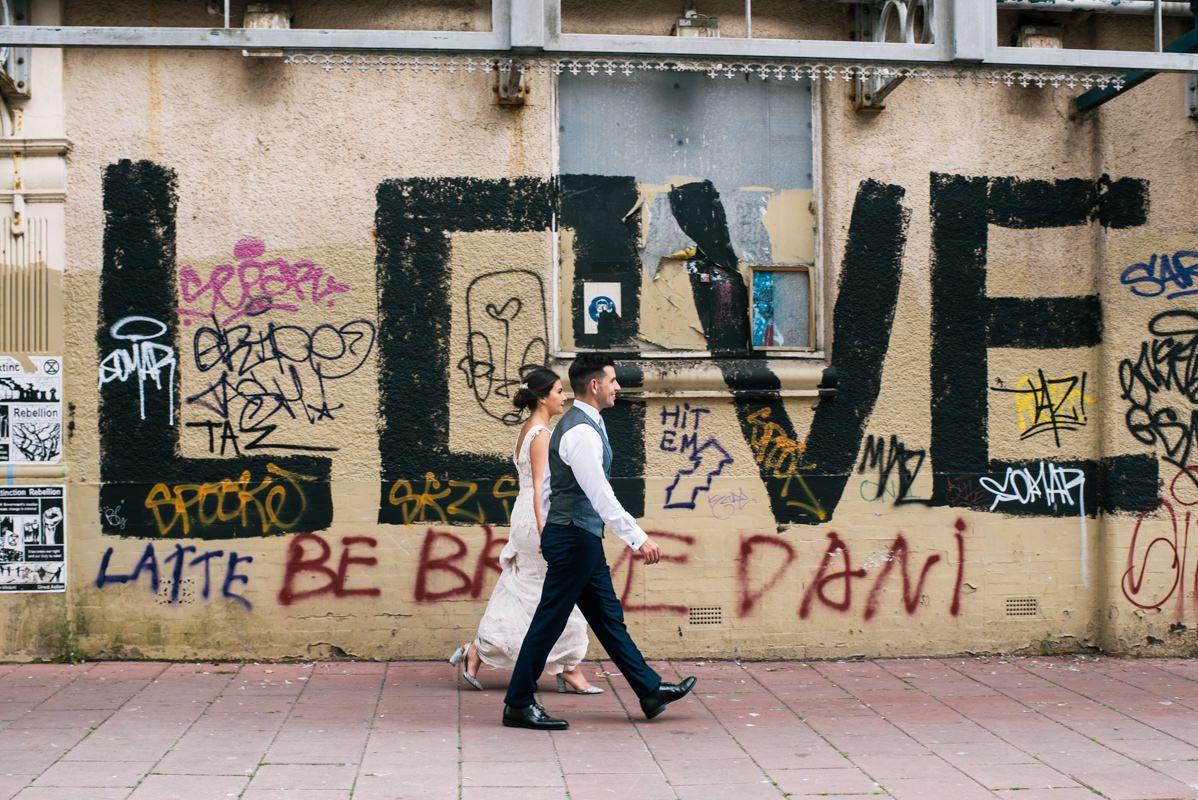 Person walks past large LOVE graffiti on urban wall during wedding photo session.